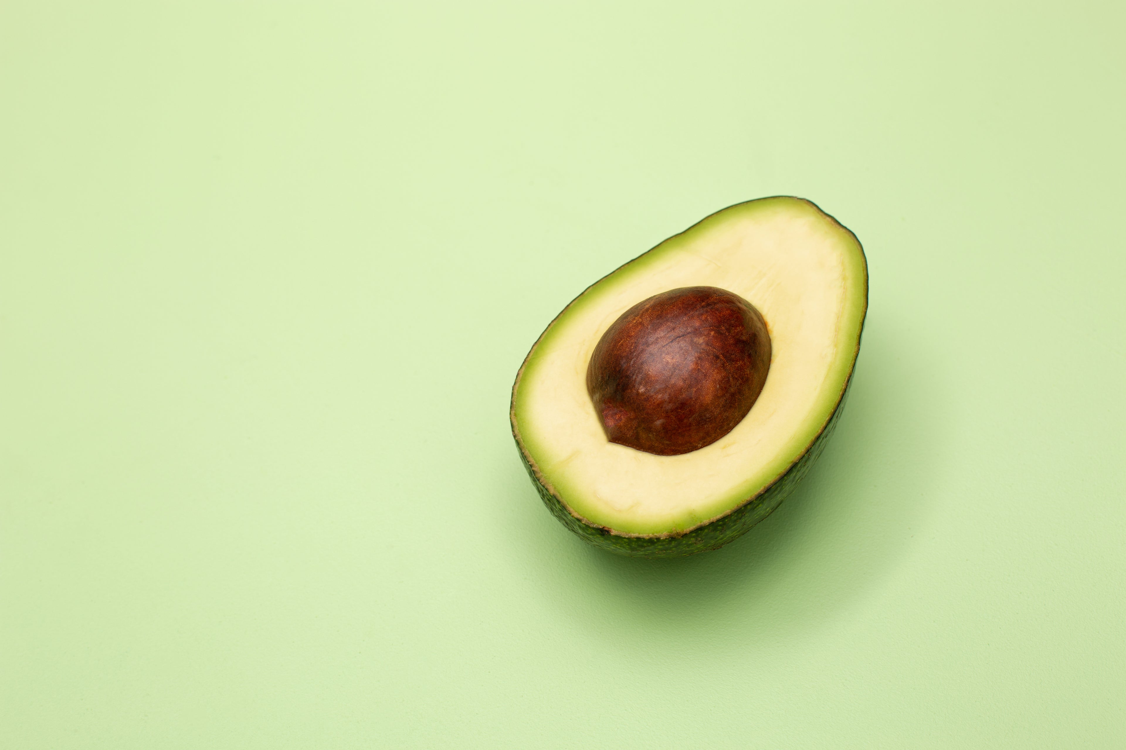 Avocado tagliato a metà su sfondo verde chiaro