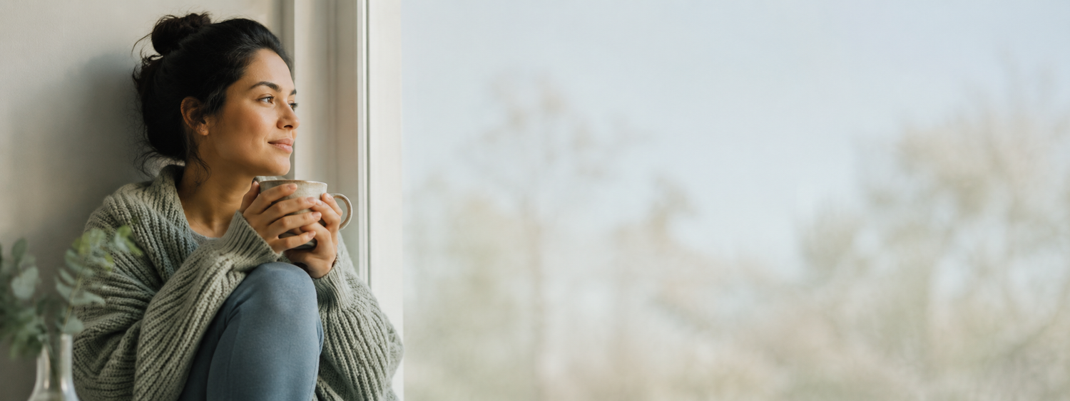 Persona alla finestra al mattino con tazza calda, energia e difese immunitarie - Nutrabiopharma